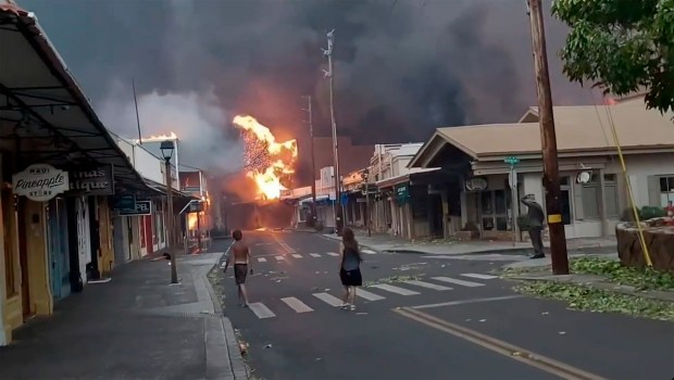 People watch as smoke and flames fill the air from raging wildfires on Front Street in downtown Lahaina, Maui on Tuesday, Aug. 8, 2023. Maui officials say wildfire in the historic town has burned parts of one of the most popular tourist areas in Hawaii. County of Maui spokesperson Mahina Martin said in a phone interview early Wednesday fire was widespread in Lahaina, including Front Street, an area of the town popular with tourists. (Alan Dickar via AP)