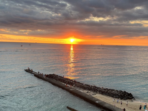Tourists watch a sunset from world-famous Waikiki. (Photo by David Dickstein)